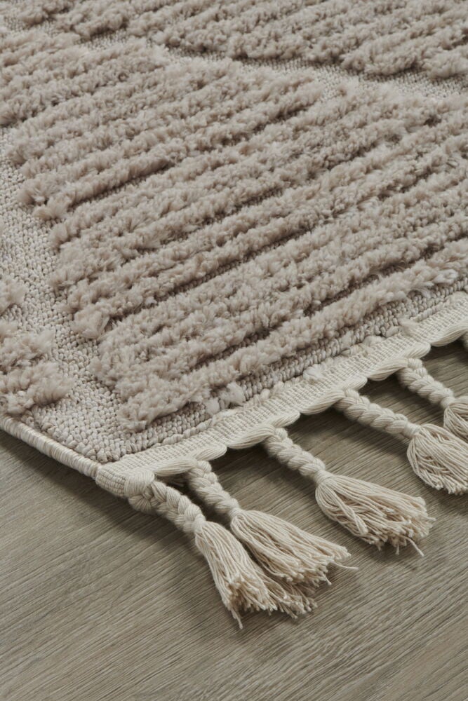 Beige maskinvävd matta med tjock lugg och fransar.