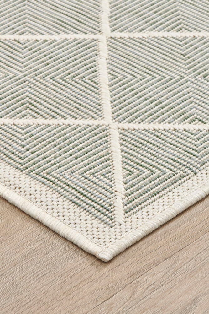 Hörnet av en grön slätvävd matta på golv.