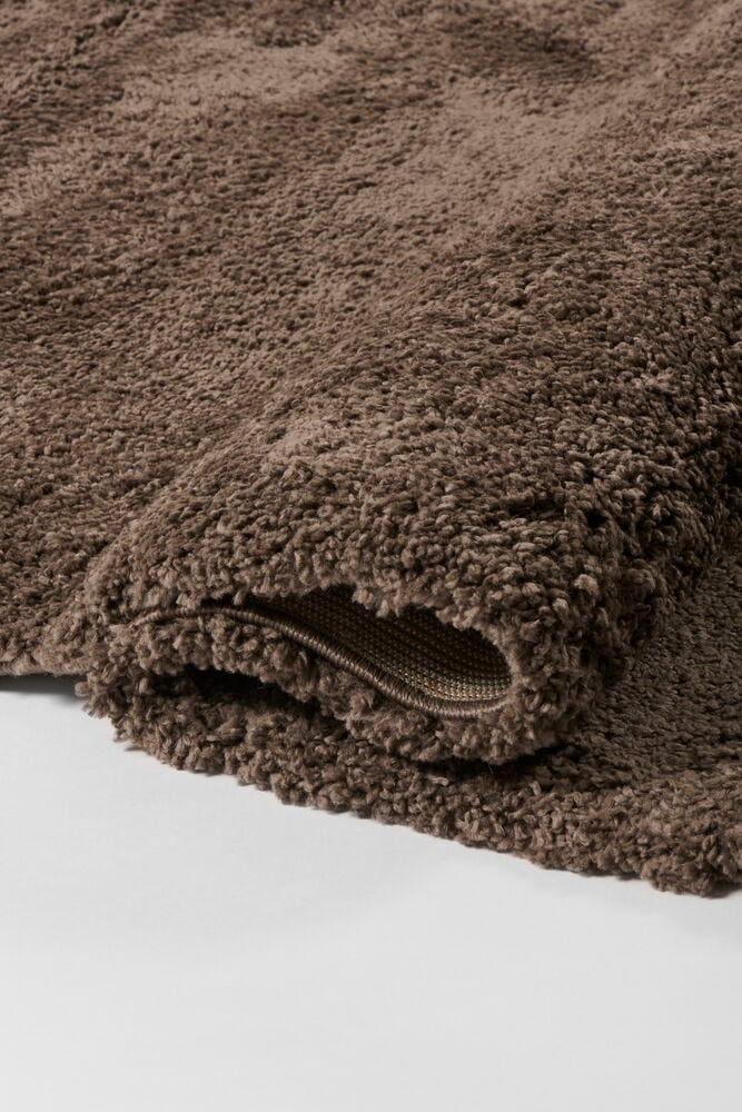 Nahaufnahme eines gerollten braunen Polypropylen-Hochflorteppichs, der seine weiche Textur und Unterseite zeigt.