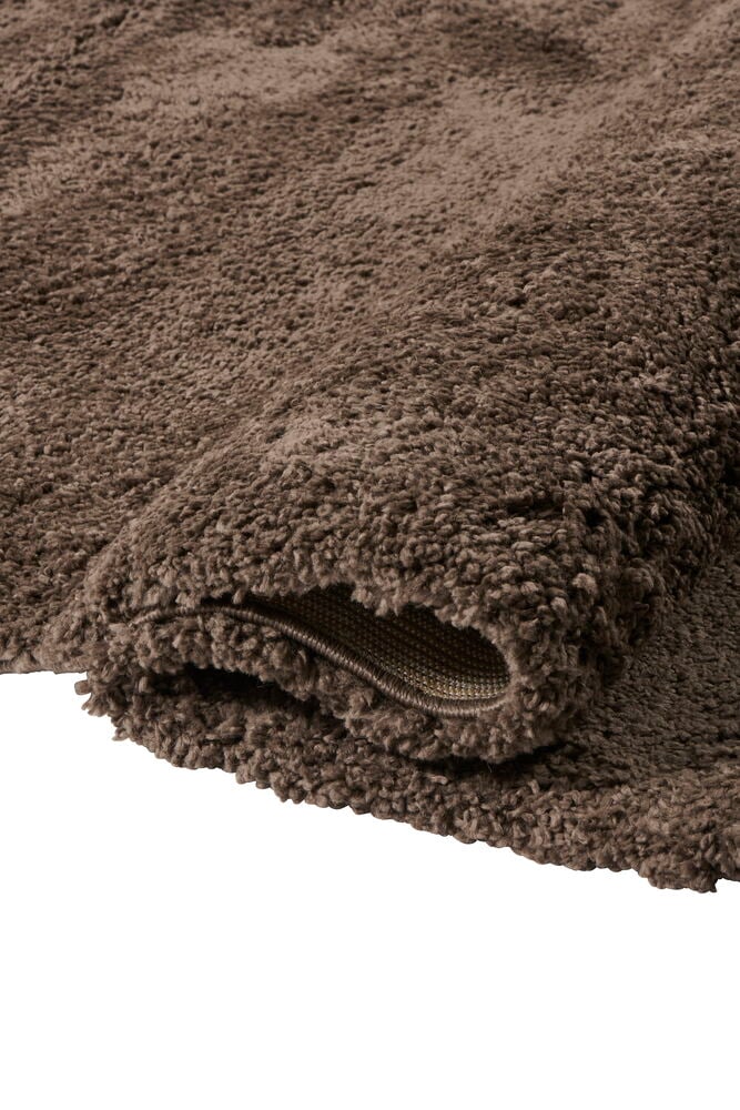 Närbild av en brun Elin matta i polypropen med lurvig textur, delvis ihoprullad.