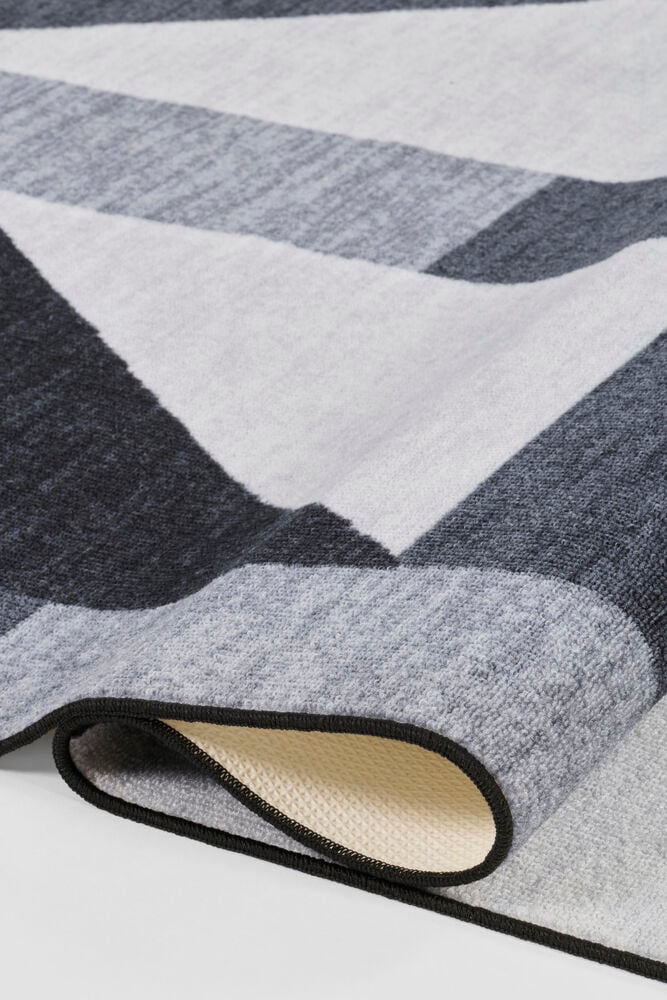 Schwarzer Polyamid Teppich Betty mit geometrischem Grau- und Weißmuster, gefaltet, um seine beige texturierte Unterseite zu zeigen.
