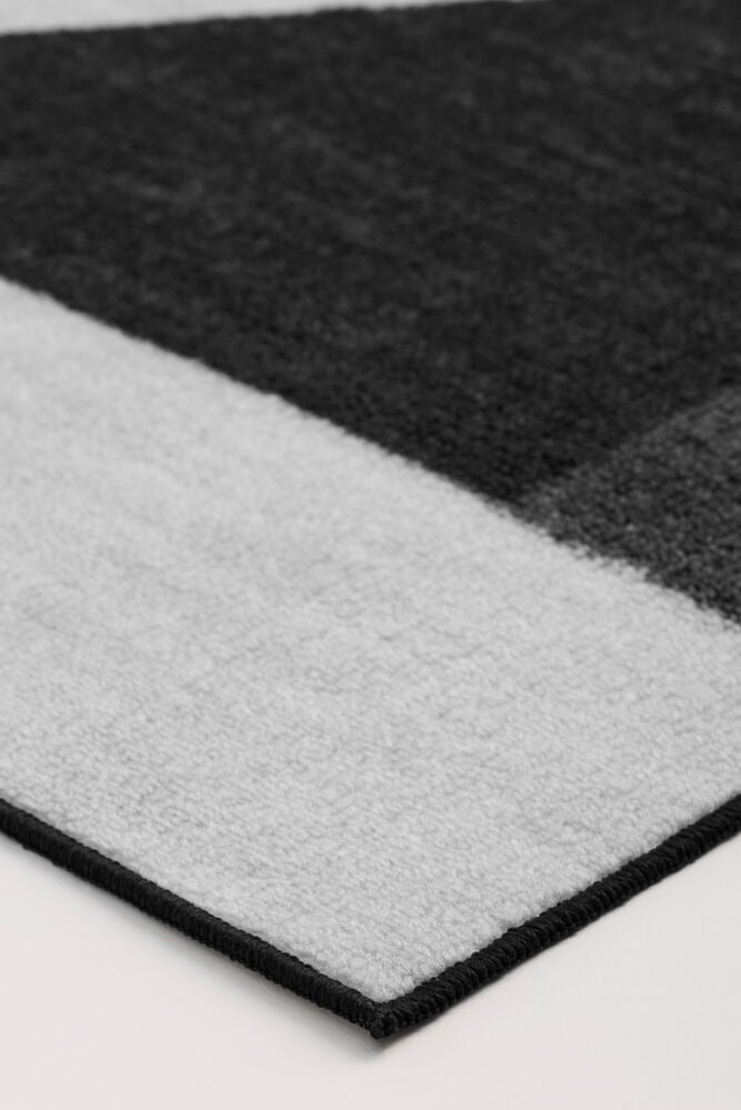 Eine Nahaufnahme eines schwarz-hellgrau geometrisch gemusterten Polyamid-Teppichs mit schwarzem genähtem Rand.