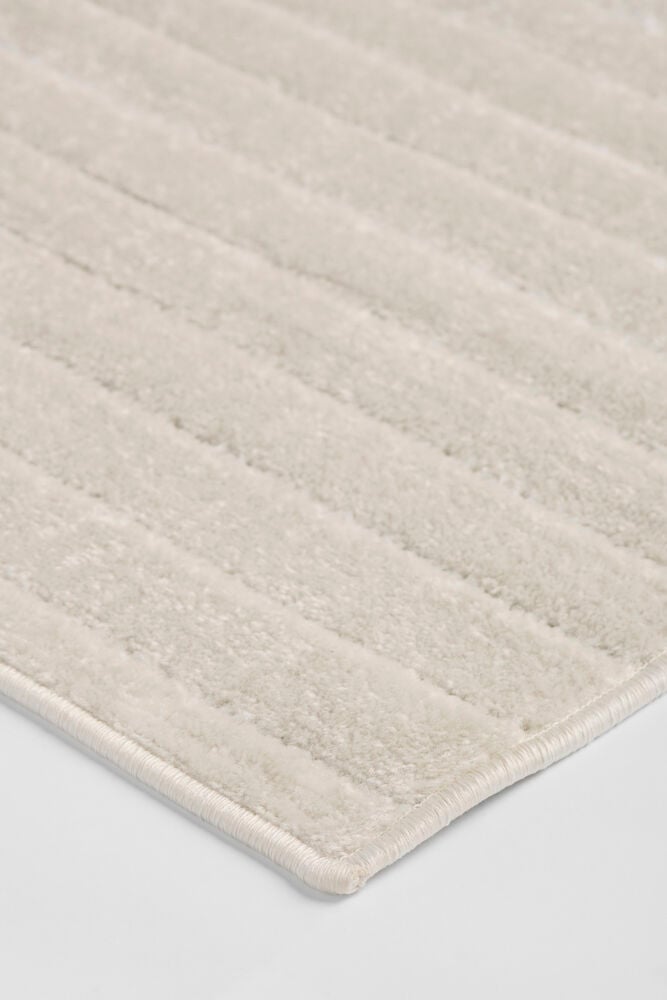 Vinklet nærbilde av et off-white polypropen teppe Billie med hevede horisontale striper og en pen kant.