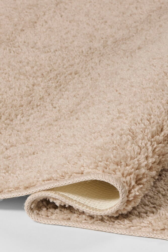 Lähikuva rullatusta Beige Polypropeeni Tilda matosta, esittäen sen pörröistä nukkaa ja kudottua taustaa.