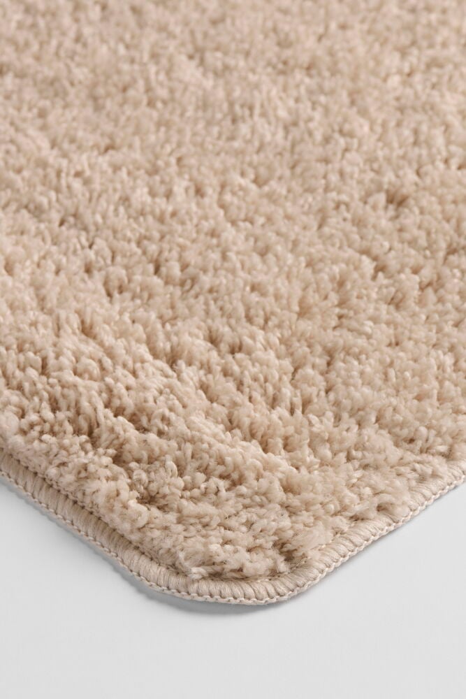Närbild av en beige lurvig Matta Tilda i polypropen, visar dess texturerade yta och sydda hörn.