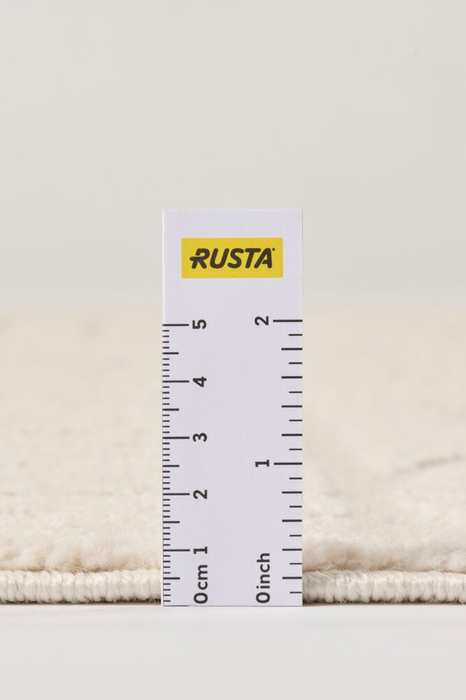 Cremefarbener Teppich Mette mit dickem, weichem Flor, dessen 2,5 cm Dicke ein Lineal zeigt.