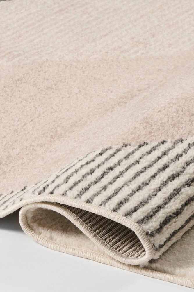 Nærbilde av et foldet beige Teppe Lina i polypropen, med grå striper og strukturert underside.