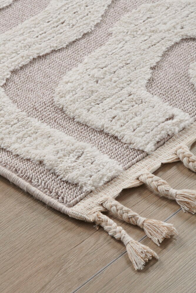 Beige matta med flätade fransar på trägolv.