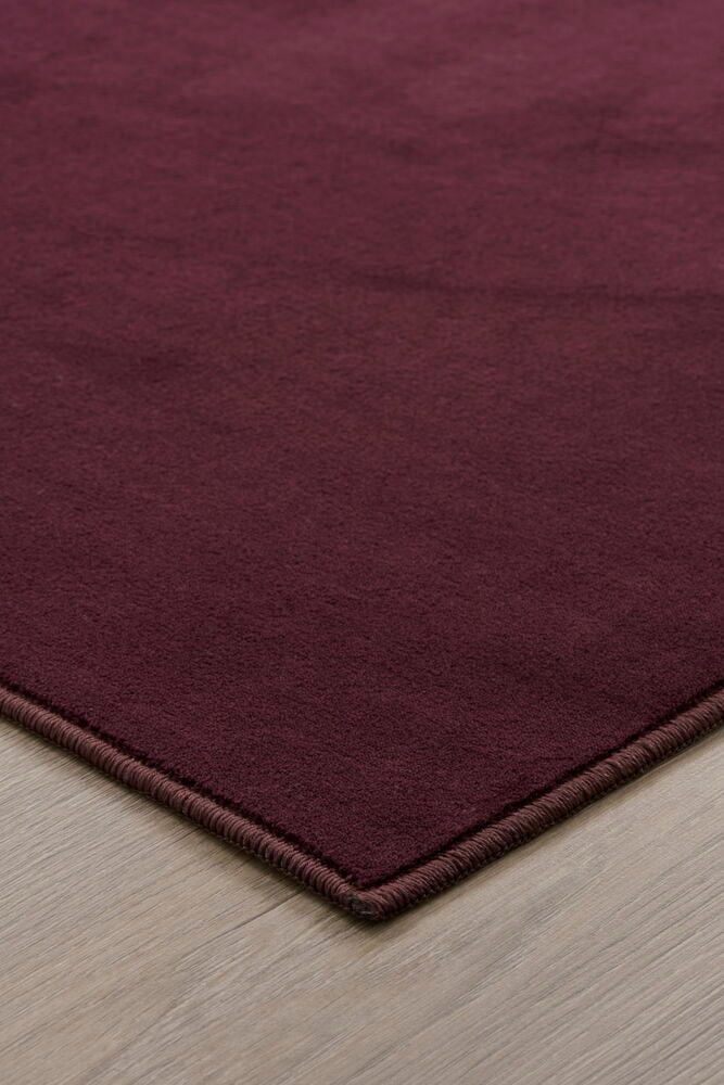 Ett hörn av en vinröd matta på golv.