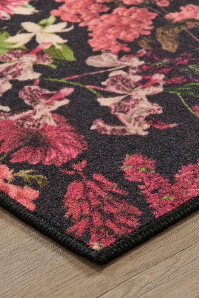 Svart matta med rosa blommönster på trägolv.