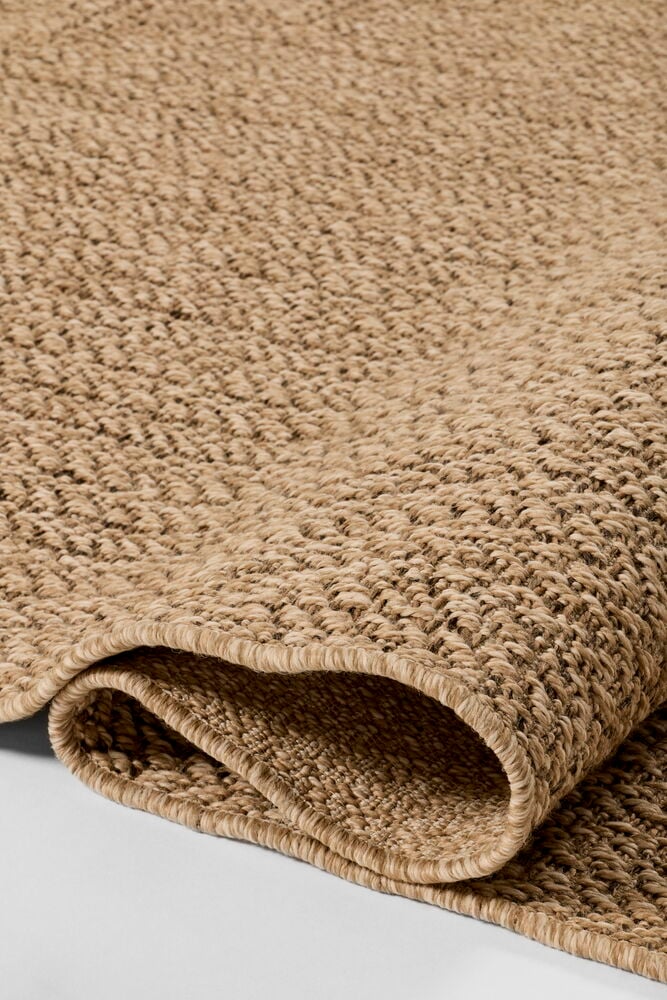 Nahaufnahme eines sandfarbenen Teppichs Katja 200x290 cm Polypropylen, zeigt gewebte Textur und gerollte Kante.