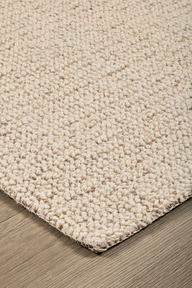 Närbild av en ljusbeige texturerad matta med en framträdande ögleslinga, med kanten på ett trägolv.