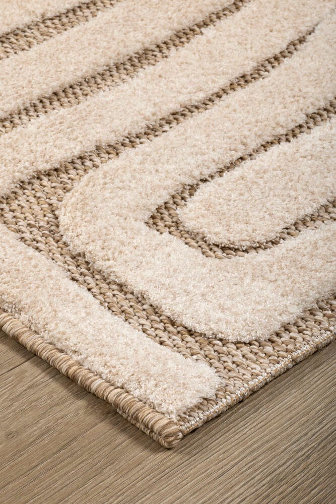 Nærbilde av et beige og kremhvitt mønstret teppe med raggete og vevde teksturer på et tregulv.