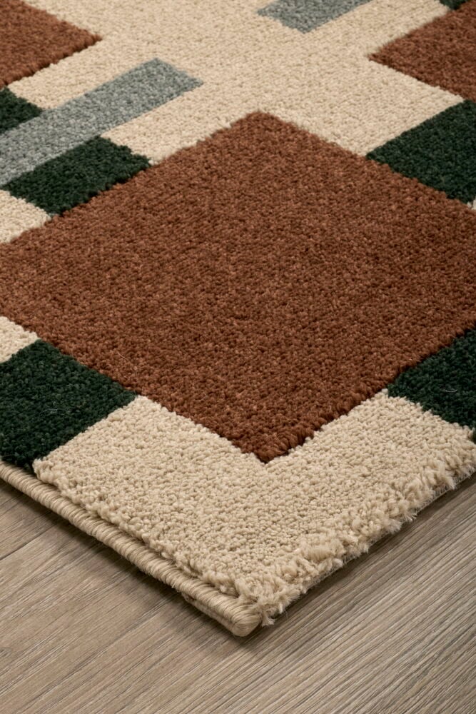 Nærbilde av Teppe Susanna, et polyesterteppe med rust, mørkegrønt, beige og blått geometrisk blokkmønster.