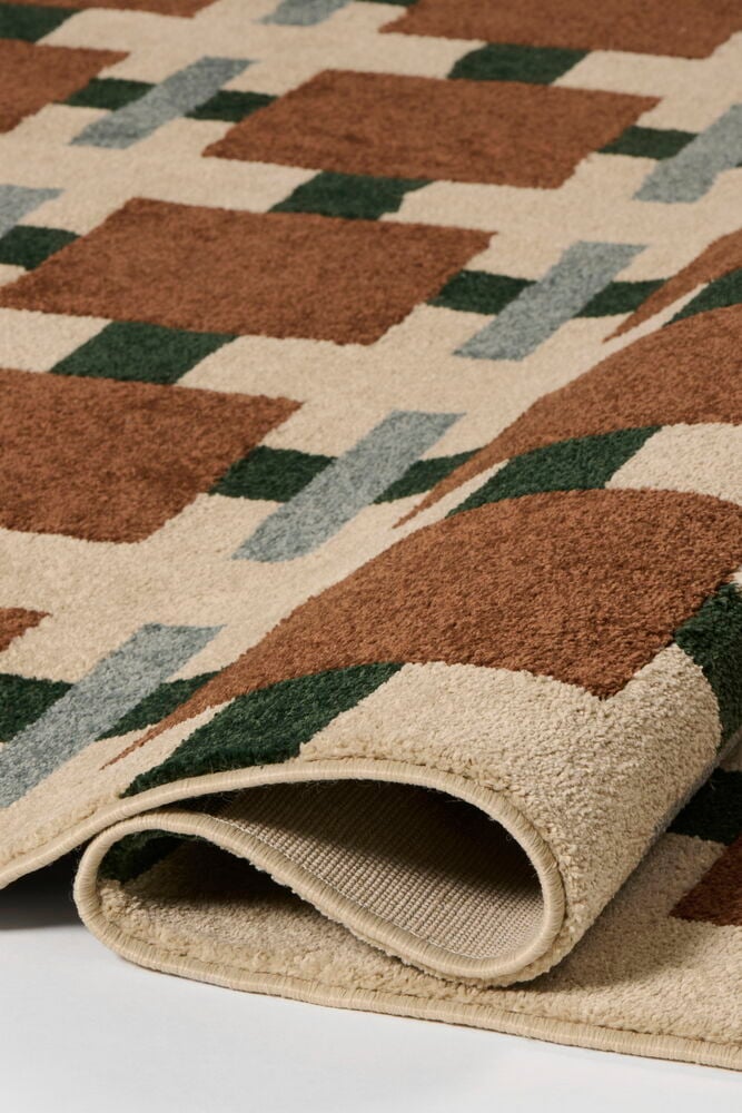 Nærbilde av delvis rullet Teppe Susanna Rust Polyester, geometrisk mønster i rust, grønt, grått, beige.