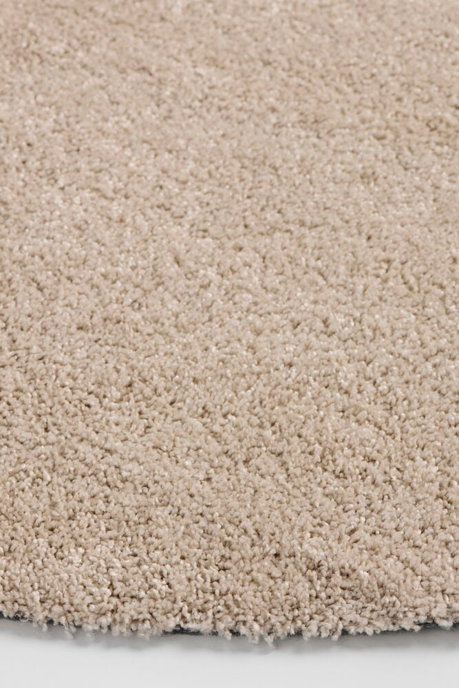 Nahaufnahme eines runden beigen Teppichs Lizette aus Polypropylen, 133 cm Durchmesser, weiche Textur.
