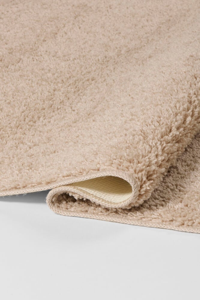 Nahaufnahme eines gerollten Beigen Polypropylen Läufers Tilda, der seine flauschige Textur und flache Unterseite zeigt.