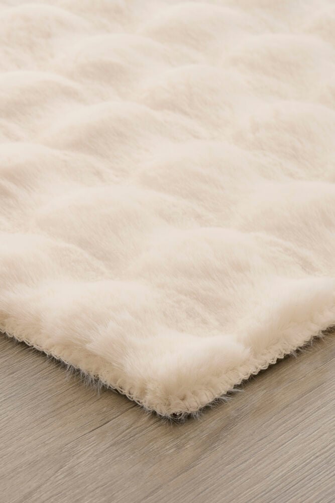 Närbild av vit fluffig matta på trägolv.