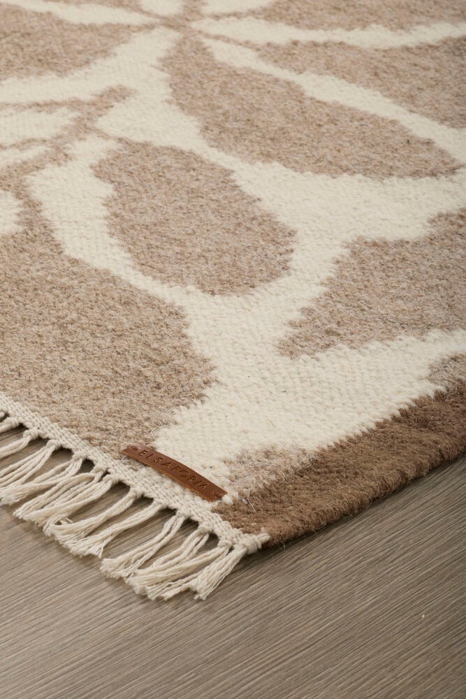 Lähikuva kudotusta Beige Villa matosta, jossa on abstrakti luonnonvalkoinen kuvio, hapsut ja merkki.
