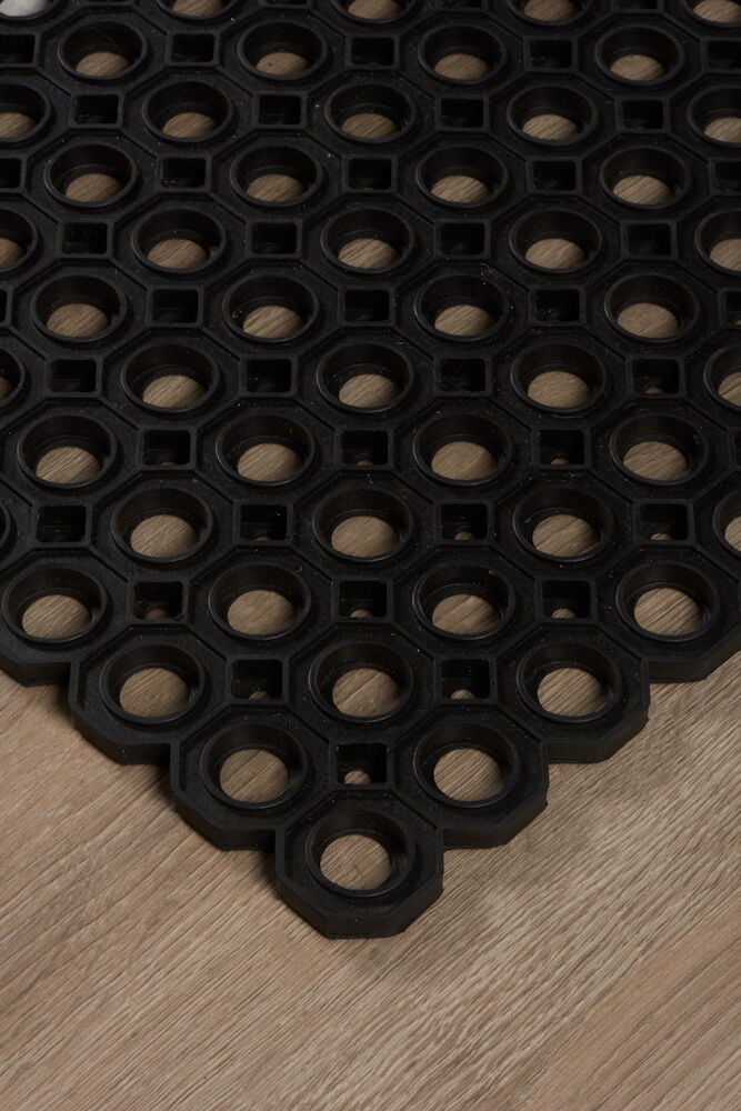 Musta kumi matto, jossa on pyöreitä reikiä puulattialla.