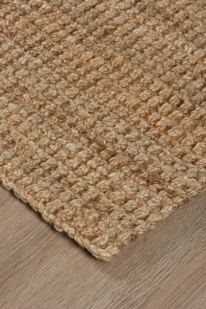 Käsinkudottu ovimatto hiekanvärisestä juutista puisella lattialla.