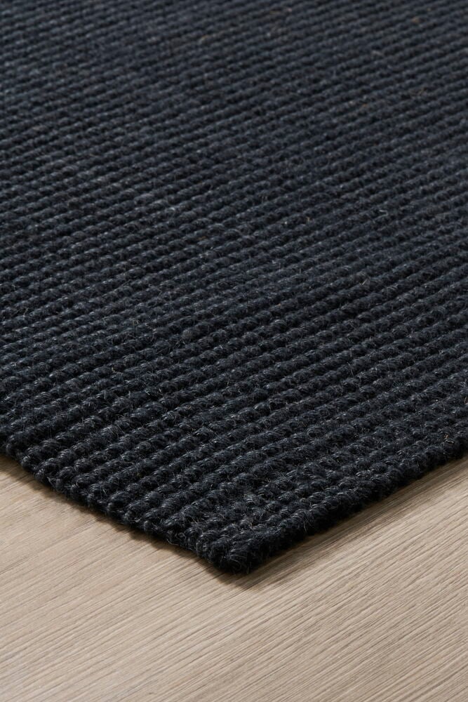 Musta ovimatto vaalealla puulattialla.