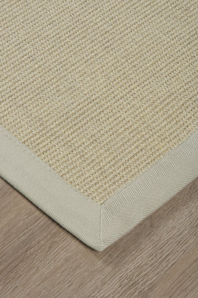 Beige dörrmatta i sisal med kant, på trägolv.