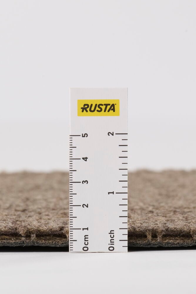 Närbild på en texturerad Grå Polyestermatta med en vit linjal som visar tjocklek i cm och tum.