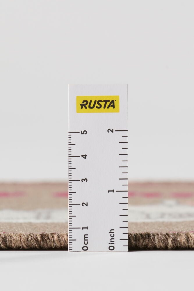 Nahaufnahme von der Seite eines beigen Polyamid-Teppichs mit rosa Muster, der etwa 0,5 cm dick ist.