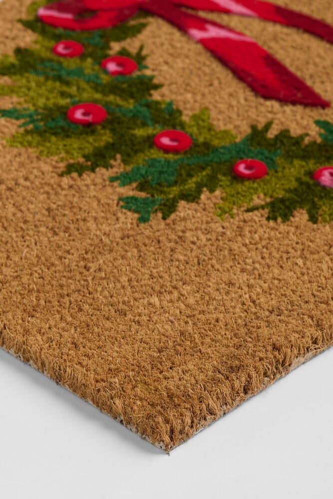 Nahaufnahme einer Natur Kokosfaser Fußmatte mit grünem Weihnachtskranz und roten Beeren.