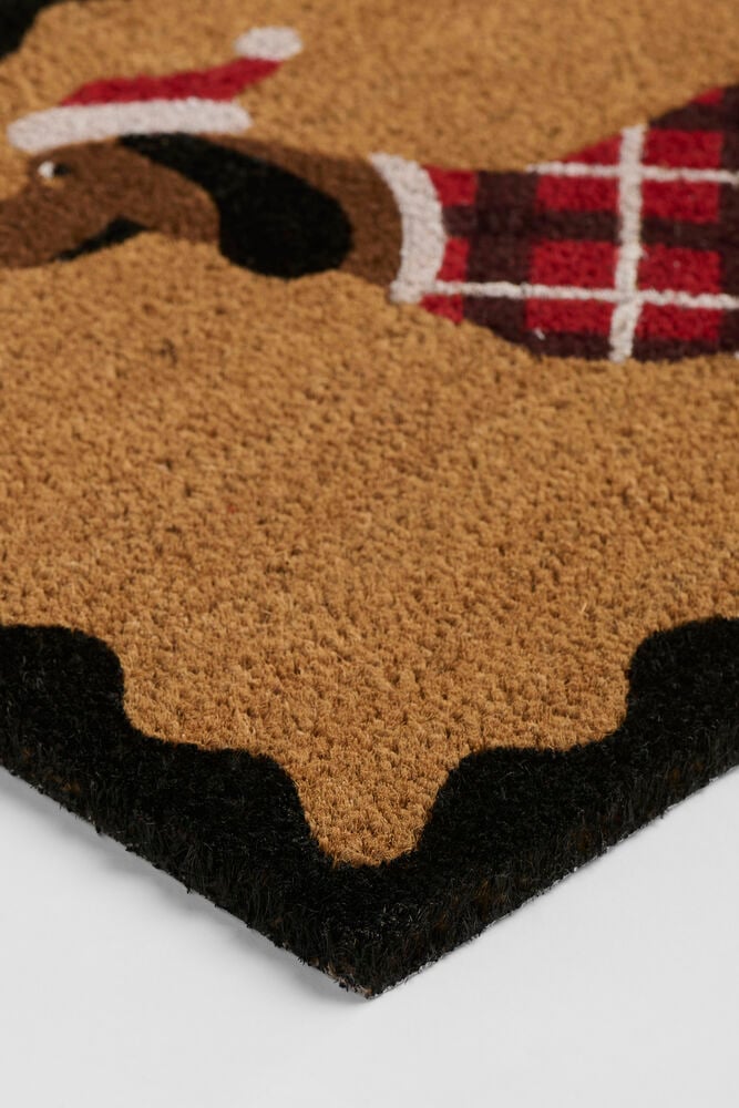 Natur Kokosfaser Fußmatte mit Dackel in roter Weihnachtsmütze und kariertem Pullover, mit schwarzem Wellenrand.