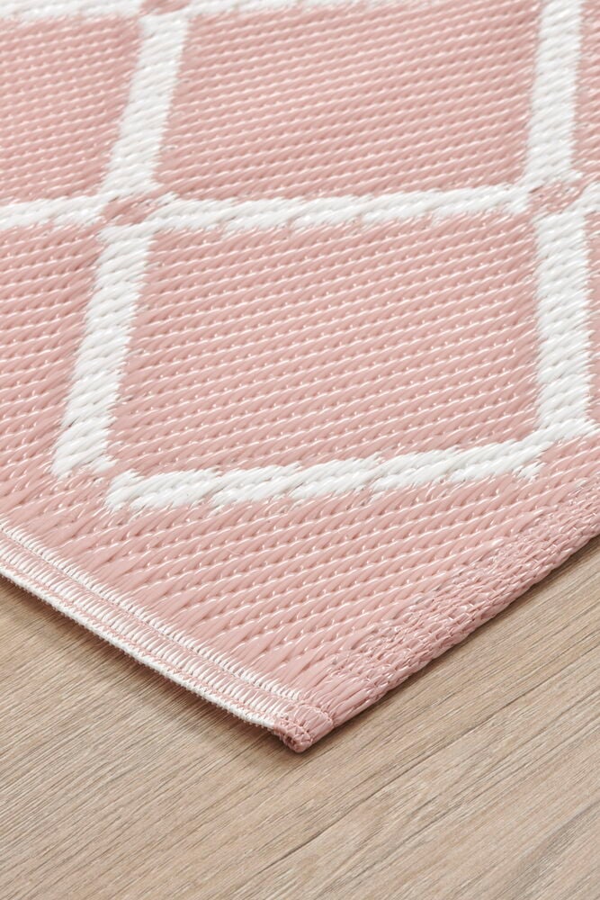 Rosa plastmatta med vitt rutmönster på trägolv.