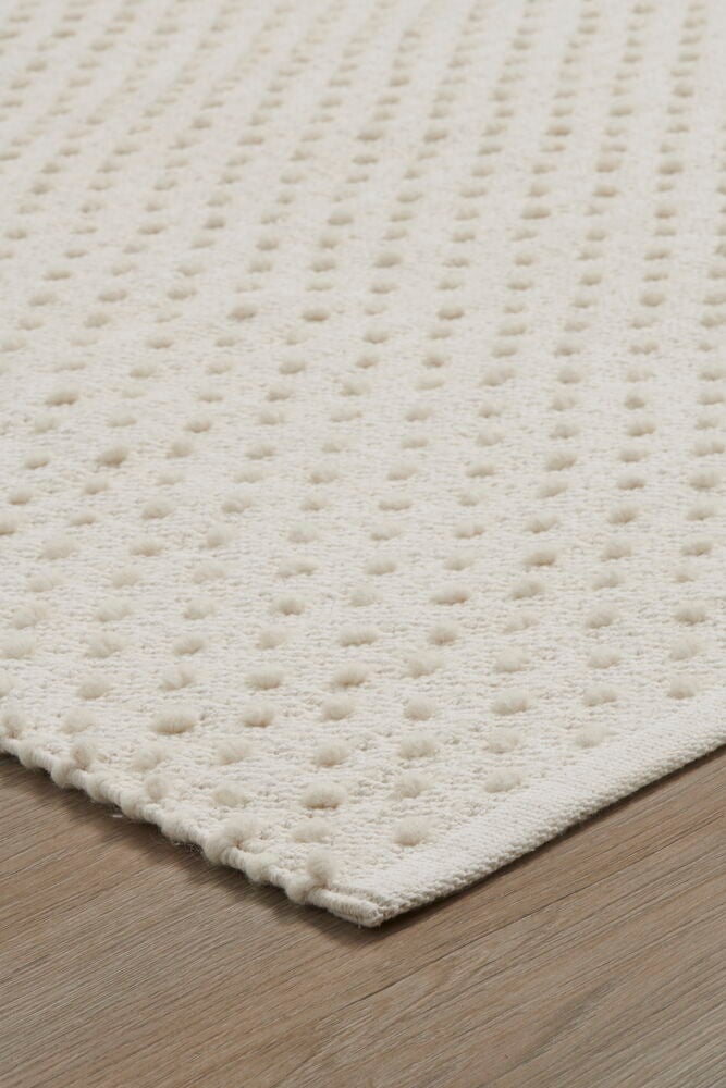Vit matta med små bollar på trägolv.