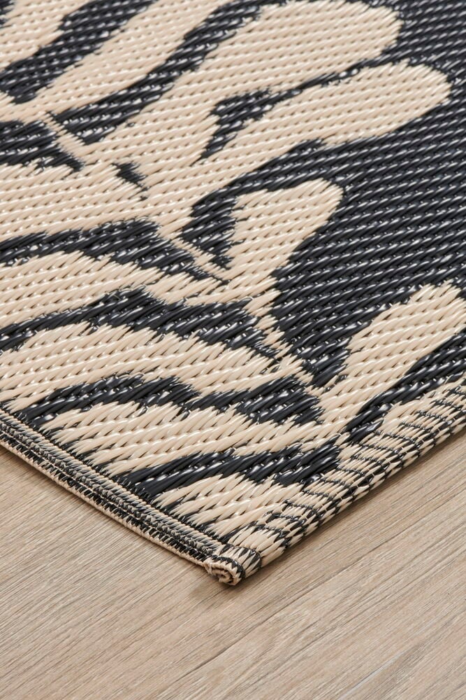 Beige polypropenmatta med svart bladmotiv på trägolv.