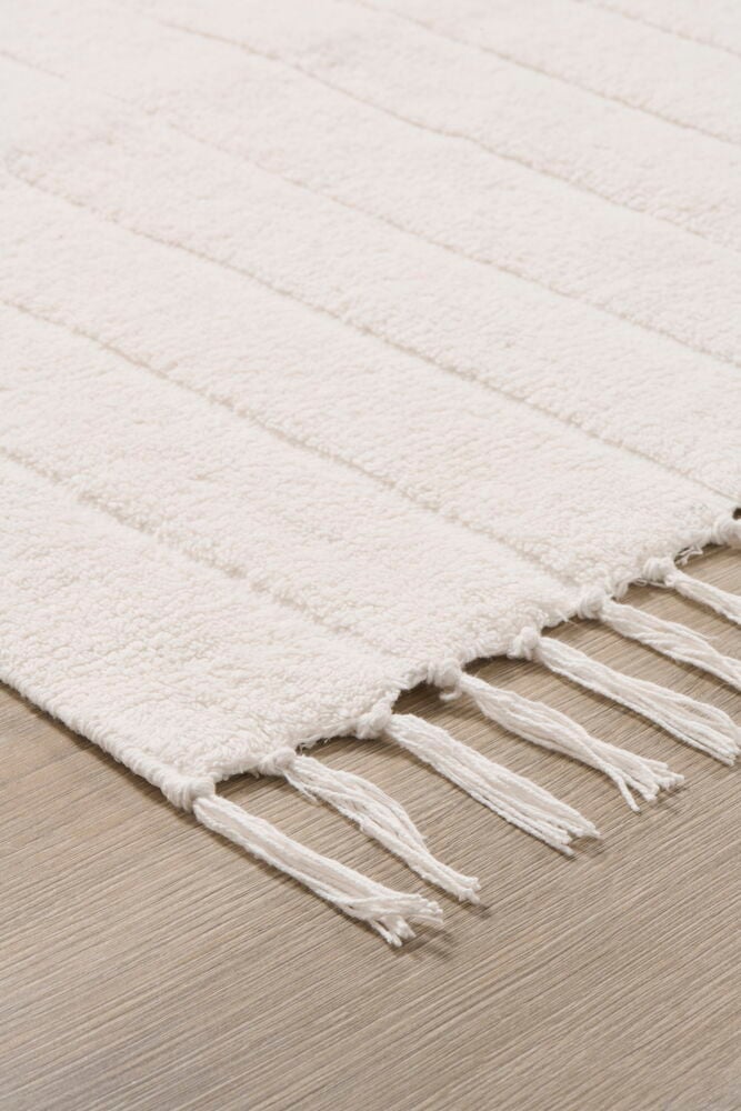 Vit bomullsmatta med fransar på trägolv.