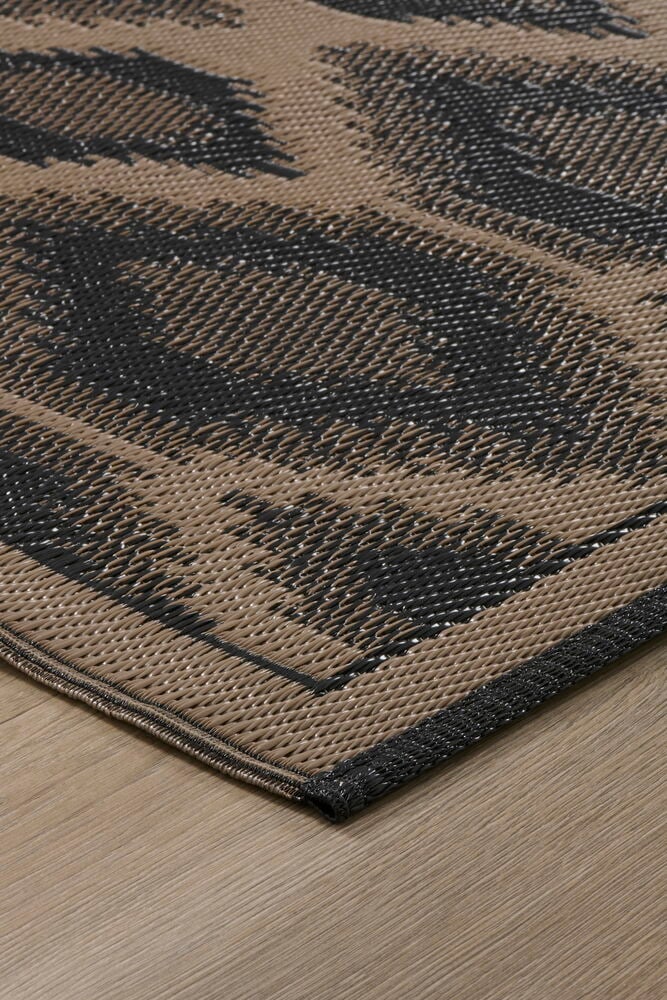 Brun och svart Inka mönstrad polypropen Bastmatta på ett trägolv, vinklad närbild.