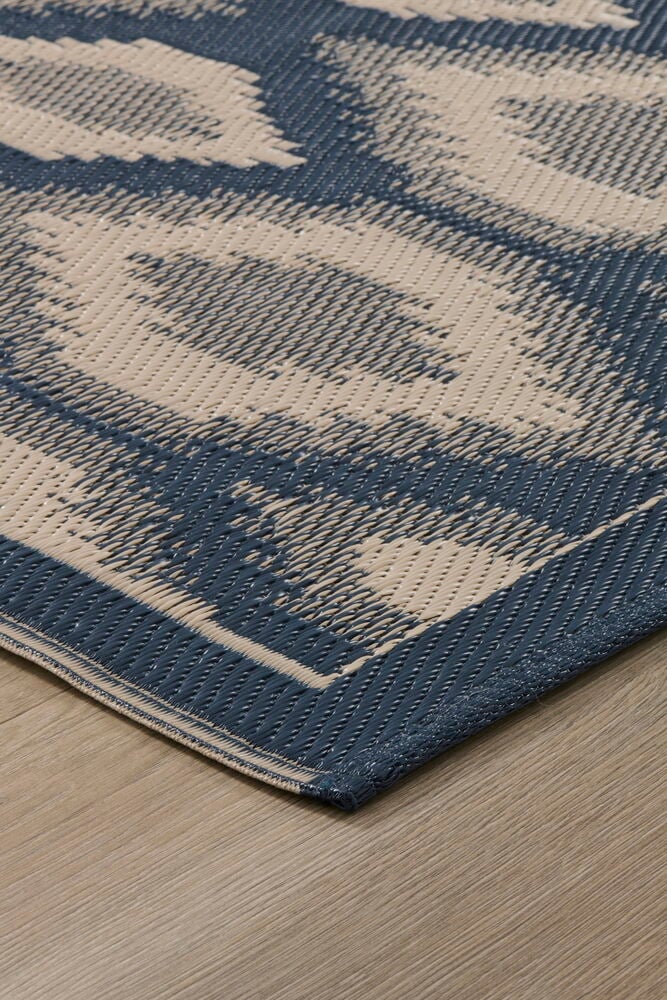 Lähikuva sinisestä ja beigestä geometrisesta Matto Inkasta polypropeenista vaalealla puulattialla.