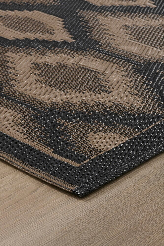 Ruskea ja musta geometrinen kudottu Matto Inka, vinossa näkymä puulattialla.