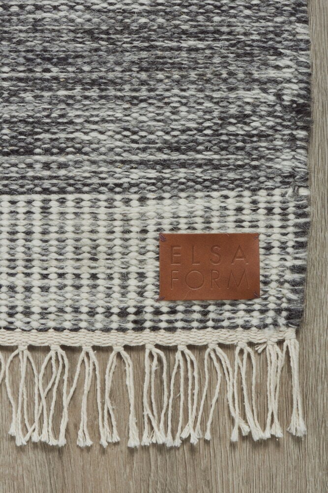 Handgewebter grauer Wollteppich mit Fransen und Lederetikett.