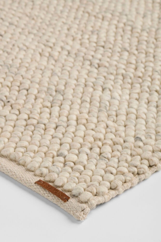 En naturfärgad matta i ullblandning med bubblig textur och en brun Elsaform-tagg.