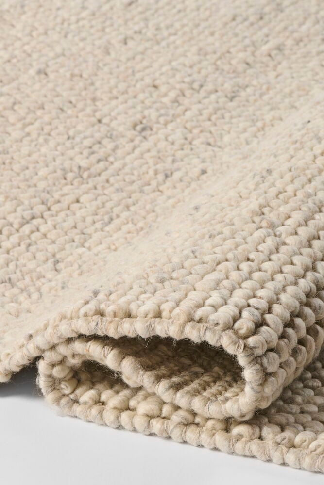 En nærvisning av et naturbeige teppe i ullblanding med en teksturert, løkket overflate, brettet.