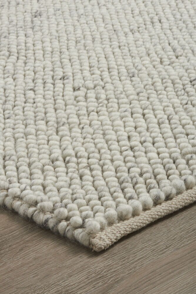 Käsinkudottu vaaleanharmaa matto pienillä huopapalloilla.