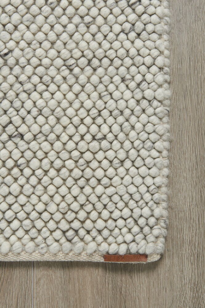 Käsinkudottu vaaleanharmaa villamatto, jossa pieniä huovutettuja palloja.
