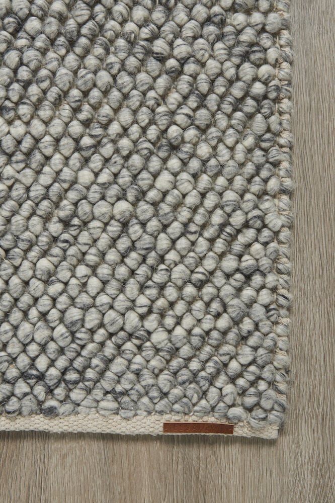 Harmaa käsinkudottu villamatto, jossa on pehmeä kupliva rakenne.