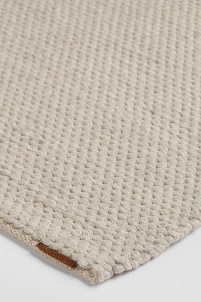 En närbild av en naturfärgad matta i ullblandning med texturerad yta och en brun läderetikett.