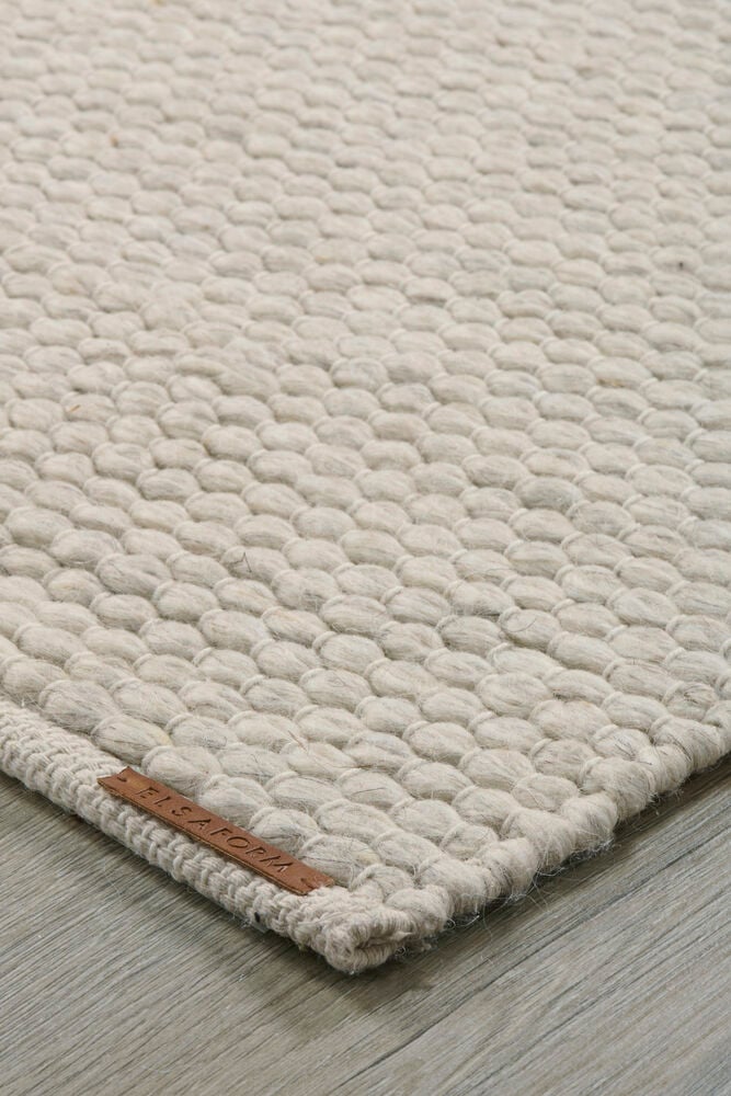 Beige handvävd matta på trägolv, närbild.