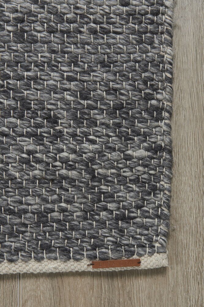 Handvävd mörkgrå ullmatta på trägolv.