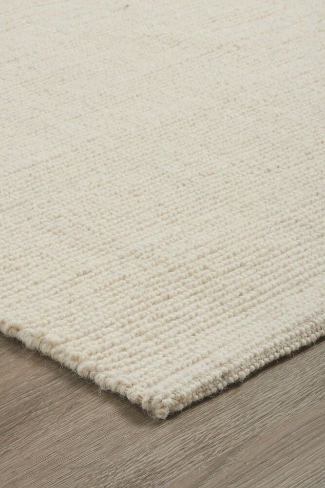 Käsinkudottu villamatto luonnonvärissä puulattialla.