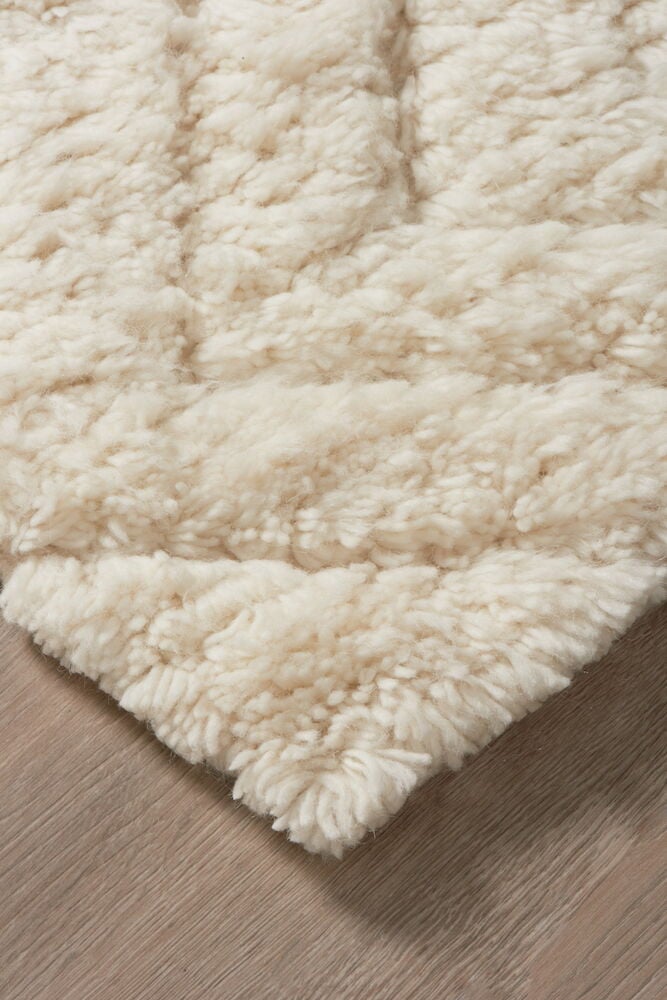 Hörn av handvävd naturfärgad ullmatta på trägolv.