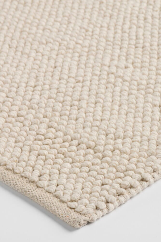 Vit Elsaform Anne gångmatta i ullblandning med texturerad, öglad yta och vävd kant.